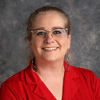 Laura Murray, Assistant to the Registrar with glasses and light hair, wearing a red collared shirt and drop earrings, in front of a gray background.