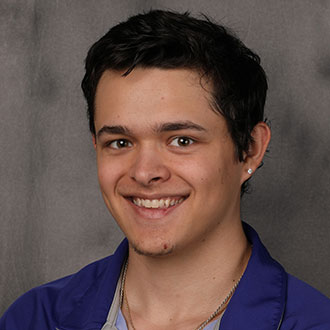 Max Nerland, Resident Hall Coordinator for the Residential Life Department, stands against a gray background.
