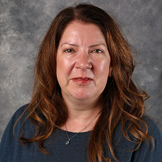 Elizabeth Olson, Associate Professor for the Business Administration Department and Taylor Leadership Institute for the Academic Affairs Department, stands in front of a gray mottled background and faces the camera.