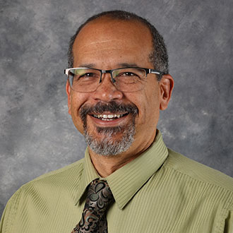 David Paulson, Assistant Professor for the Music Department, poses against a gray backdrop.