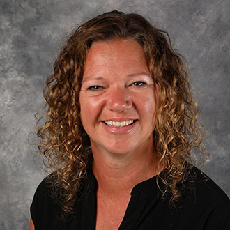Kristi Ringen, Academic Resource Center Coordinator of the Academic Affairs Department, smiles in front of a gray textured background.