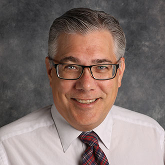 Shawn Stafford, Assistant Professor of the Religion Department, stands in front of a gray textured background.