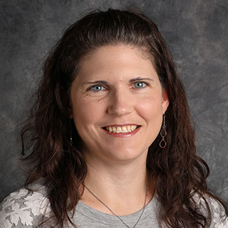 Amanda Stahl, Event Coordinator of the Advancement Department, stands in front of a gray textured background.