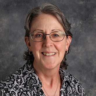 Leanne Stob, Assistant Professor of the Physics/STEM Department, poses against a gray background.