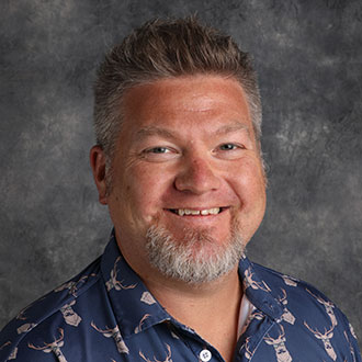 Greg Vandermause, Manager of the Production Studio Department, stands against a gray textured background.
