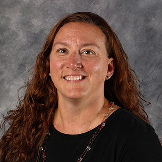 Estelle Vlieger, Director of Admissions for the Admissions Department, stands in front of a gray textured background.