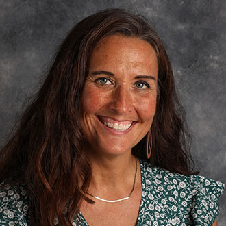 Denice Woller, Adjunct Faculty of Studio Art Department, smiling in front of a gray mottled background.