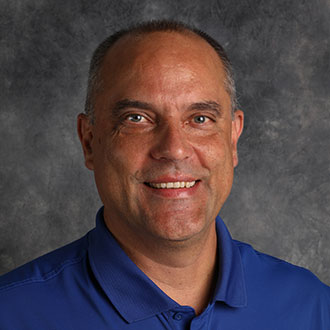 Eric Woller, Professor of the Chemistry Department, posing in front of a gray textured background.