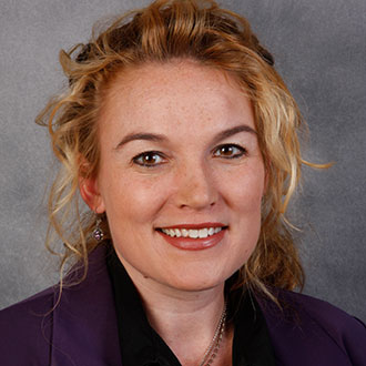 Tiffany Young Klockziem, Professor of Health & Human Performance, smiling in front of a gray background.