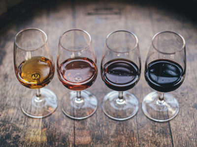Four glasses of white, rosé, red, and dark red wine on a wooden surface.