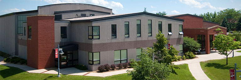 Bethany Lutheran Colleges modern two-story academic building, featuring large windows and surrounding walkways, welcomes students amid leafy trees on a sunny day in Mankato.