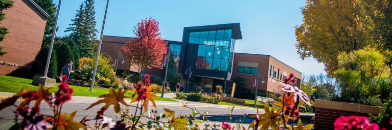 A modern brick building with large windows at Bethany Lutheran College, surrounded by vibrant trees and blooming flowers, provides a welcoming academic environment for students.