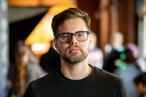 A man with short brown hair, a beard, and glasses stands indoors at Bethany Lutheran College among students.