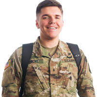 A U.S. Army serviceman, wearing a uniform and backpack, is smiling and facing forward on the campus of Bethany Lutheran College in Mankato.