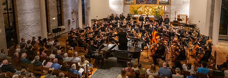 Concert band and orchestra performing in large chapel space with audience.