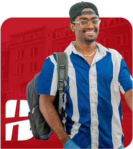 Smiling male college student wearing glasses, a backward cap, and a blue-and-white striped shirt, with a backpack over one shoulder, standing in front of a red background with a faded academic building and white "B" logo.