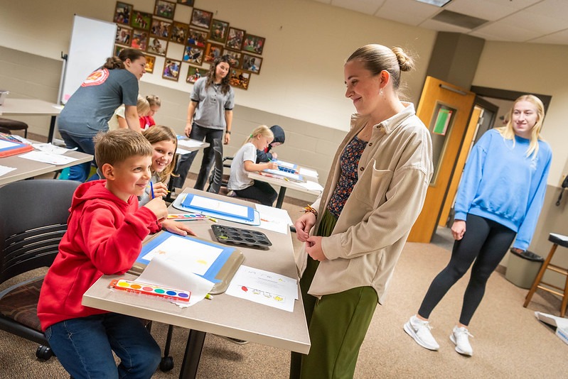A photo of two young children painting a picture with a Bethany education major looking on.