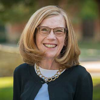Woman smiling, wearing glasses, a black sweater, and a gold necklace.