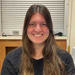 Person seated indoors with a wooden counter and metallic rolling shutter in the background.