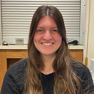 Person seated indoors with a wooden counter and metallic rolling shutter in the background.